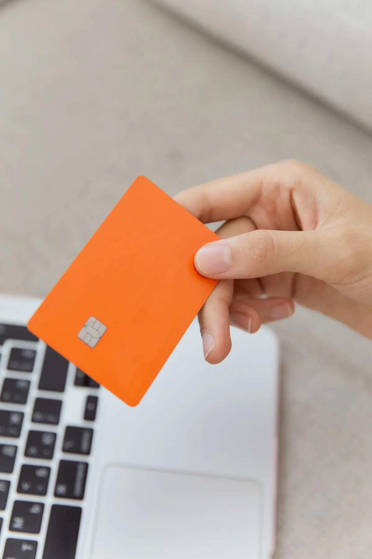 Hand holding an orange bank card above a laptop keyboard